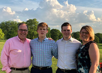Runge family standing outside in dress clothes, with greenery and a blue sky behind them, smiling 