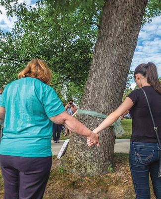 women join hands around tree with teal ribbon