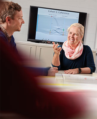 Professor Melanie Cooper sits at a table with a student. There is a graph displayed on a large TV screen behind them.