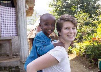 Clare O'Kane smiles and gives a piggyback ride to a young Tanzanian boy, who is also smiling.