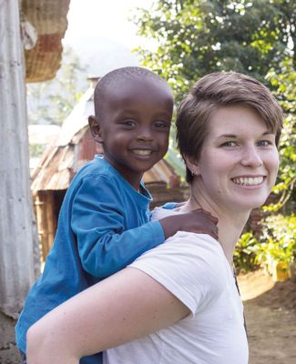 Clare O'Kane smiles and gives a piggyback ride to a young Tanzanian boy, who is also smiling.