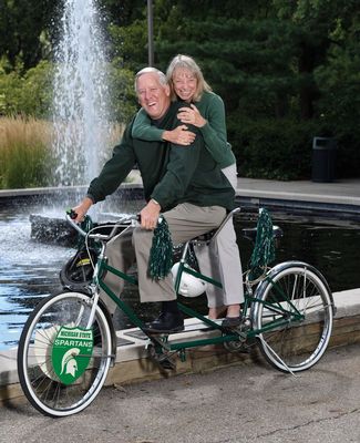 Cliff and Sue Haka pose with their bicycle in front of the MSU Library fountain
