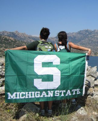 Image shows two students looking at a mountain with a MSU flag behind them.