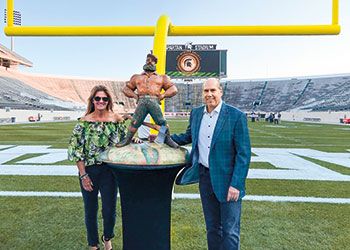 Dawn and Greg Williams posing with the Paul Bunyan Trophy in Spartan Stadium