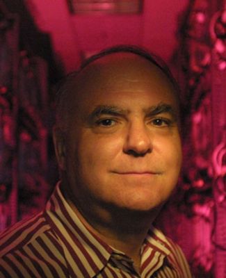 John R. Koza wears a striped shirt and stands in a pink-lighted hallway full of computer circuit boards.