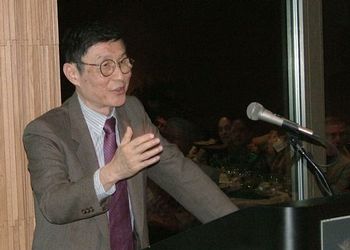 The late Professor Tung stands at a podium and speaks into a microphone.