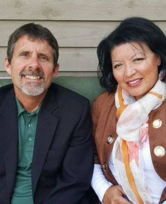 Craig and Mary Helen Crooks, dressed in blazers, sit on a bench outdoors.