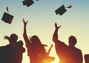 Silhouette of a group of graduates tossing caps in the air with sun shining in the background