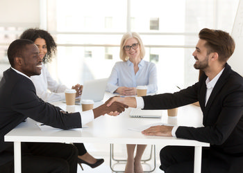 Smiling diverse business partners shake hand closing deal at office meeting