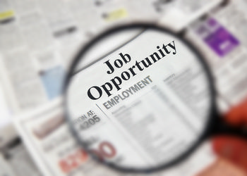 A magnifying glass focuses on the job opportunity/employment section of a newspaper