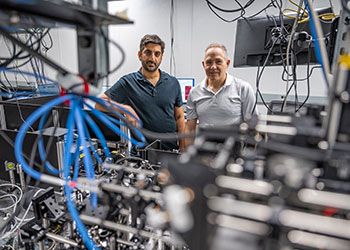 Elad Harel and Marcos Dantus pose behind cables and optical equipment in a lab space.