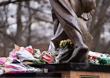 Spartan statue with bouquets of flowers laid at feet