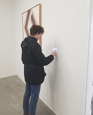 a young man touches an interactive display card on the wall at the art museum
