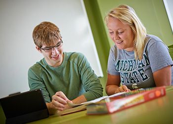 Two MSU students seated at a table studying a book.