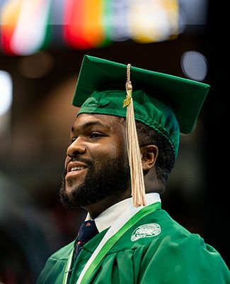 Darryl Ervin in green graduation robes, speaking at commencement