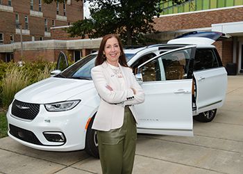 Five people stand in front of a white Chrysler minivan. 