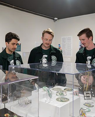 MSU students in Marching Band jackets engage with a collection of Marching Band ephemera at the MSU Museum