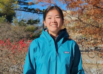 Jessica Beach in a blue jacket standing outside in front of trees