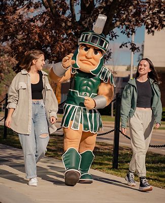 Two MSU students walking on campus with Sparty.