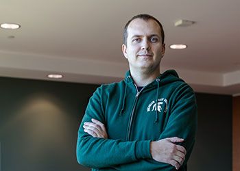 MSU student Dmytro Shynkaruk stands with his arms crossed, wearing an MSU sweatshirt and a determined expression on his face.