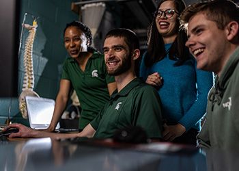 Four MSU students smiling, working in a lab together.