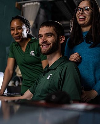 Three MSU students smiling, working in a lab together.
