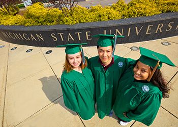 Three MSU graduates smiling, looking up at the camera.