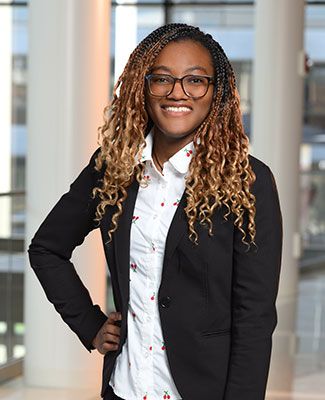 Oluwabusola Ajagbe wears a blazer and a flowered blouse and poses in a light-filled space in a campus building.