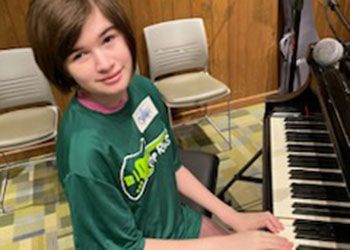 A young music therapy camp attendee sits at a piano.