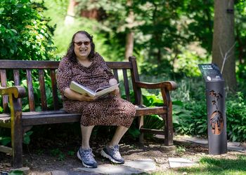 Rachel Crandall-Crocker on a bench outside on campus holding a book