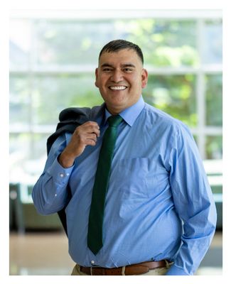 Felipe smiling on campus holding his suit jacket over his shoulder