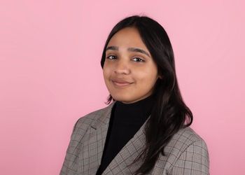 Rijul Mahajan in a blazer and black turtleneck in front of a pink background.