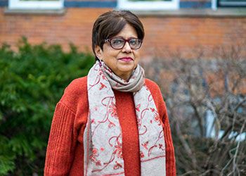 portrait of jyotsna singh, a woman in glasses wearing a red-orange sweater and a white scarf