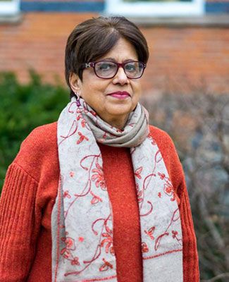 portrait of jyotsna singh, a woman in glasses wearing a red-orange sweater and a white scarf