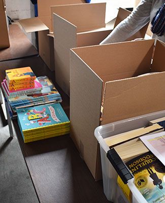 A person whose face is not visible packs colorful books into a cardboard box