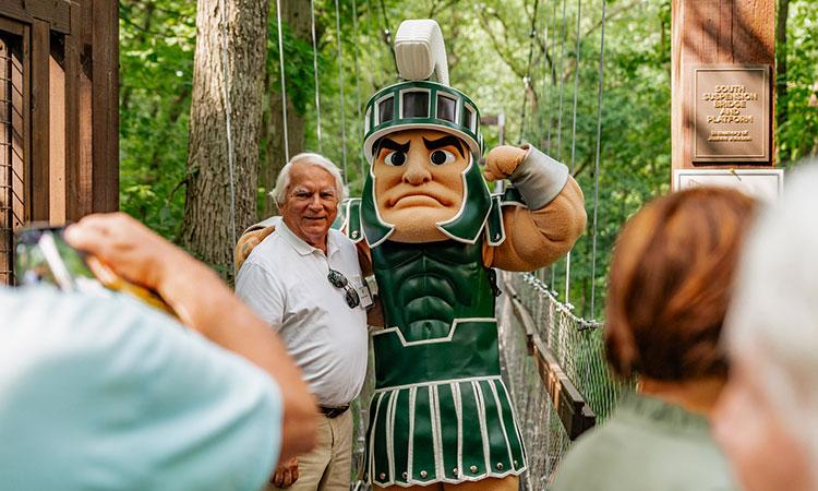 Sparty poses with a man on the Canopy Sky Walk at Hidden Lake Gardens.