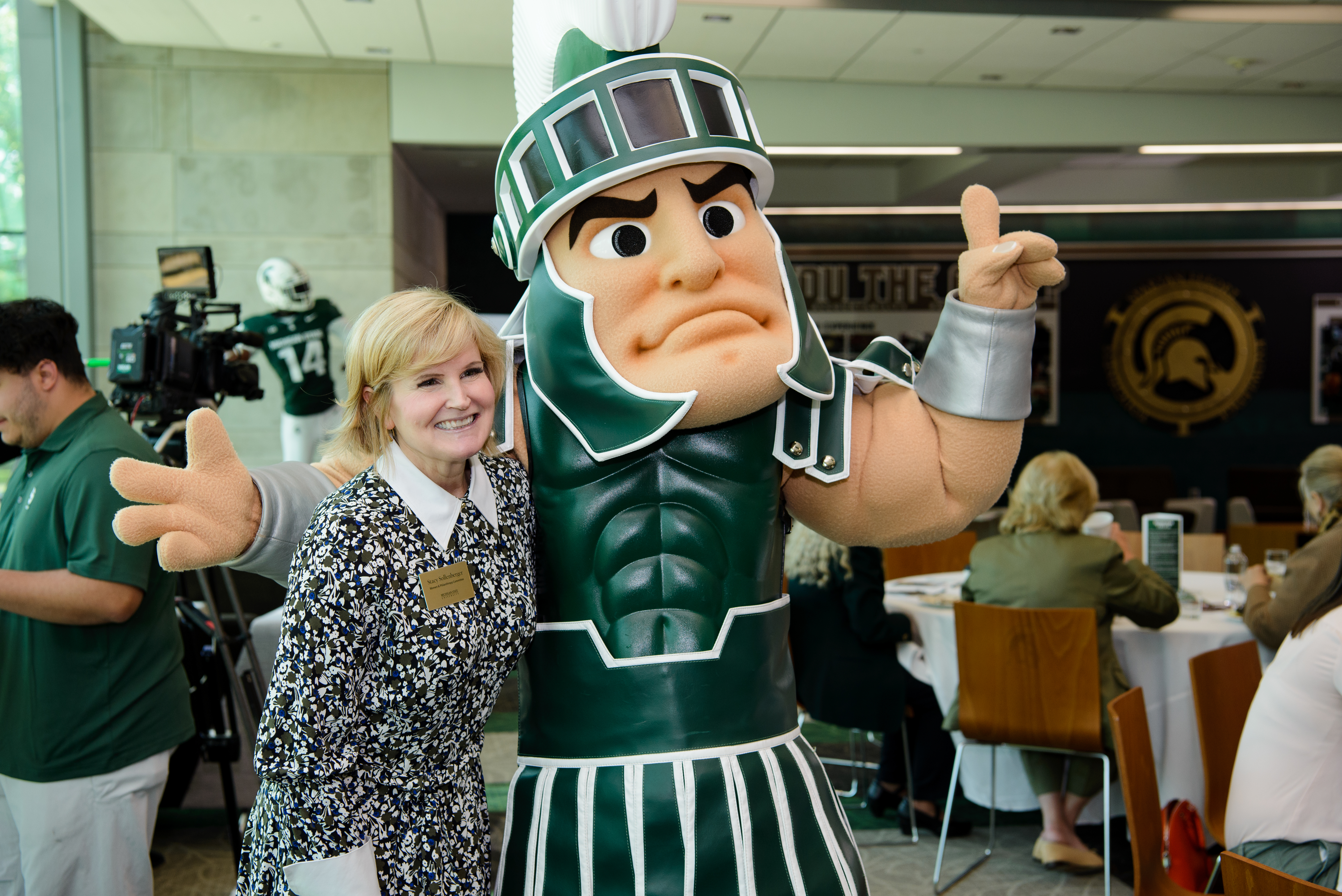 Stacy Sollenberger smiles at the camera with Sparty at an MSU campus event.