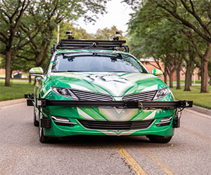 Green and white autonomous car driving down tree-lined street