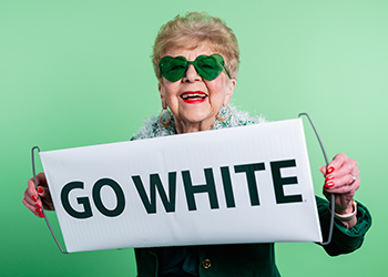 Elderly woman wearing green heart-shaped glasses holding banner that says "Go White"